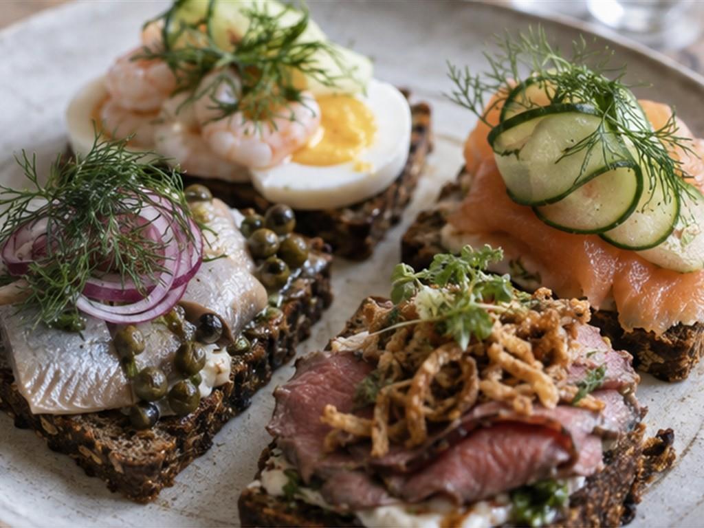 Mỗi lát smørrebrød là một tổ hợp cân bằng giữa bánh đen, phần phủ và rau thơm.